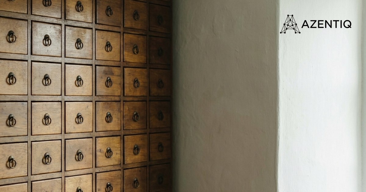 A wall of small closed wooden drawers with brass ring pulls in a goldsmith's workshop, beside a plain lime-washed wall
