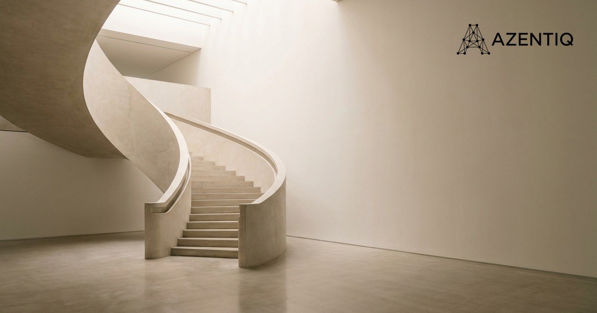 A pale curved concrete staircase rising through an empty, softly lit atrium, with a large plain wall beside it
